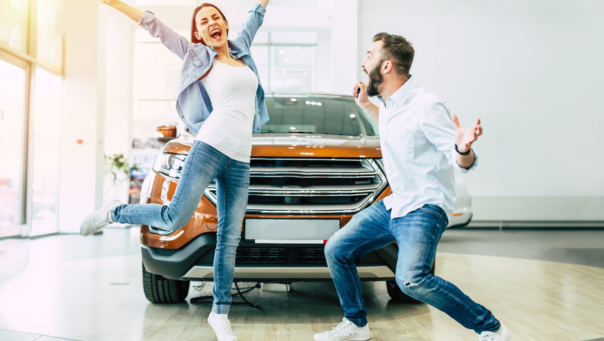 A young couple jump in excitement after buying a car at a dealership