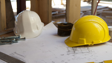 Two hard hats sitting on top of blueprints at construction site.
