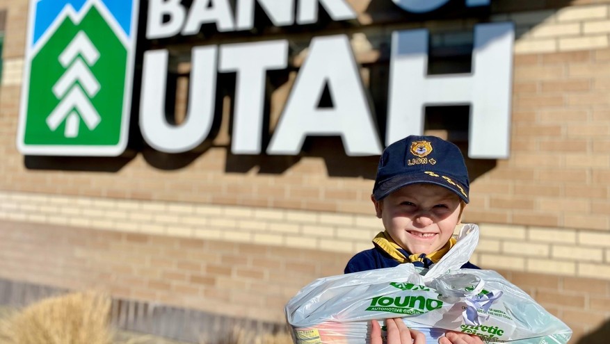 A Boy Scout is seen with a Scouting for Food bag in front of a Bank of Utah location