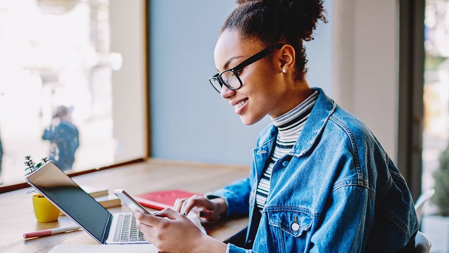 A young woman happily works digitally, with her laptop computer and a mobile phone