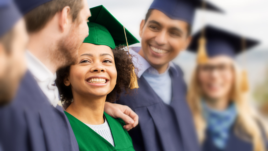 A group of high school graduates happily smile in their caps and gowns