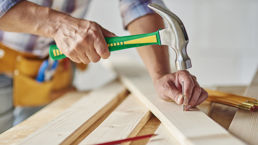 A man hammers a nail into a piece of wood