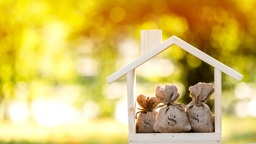 Three money bags sit inside a small wooden house figure