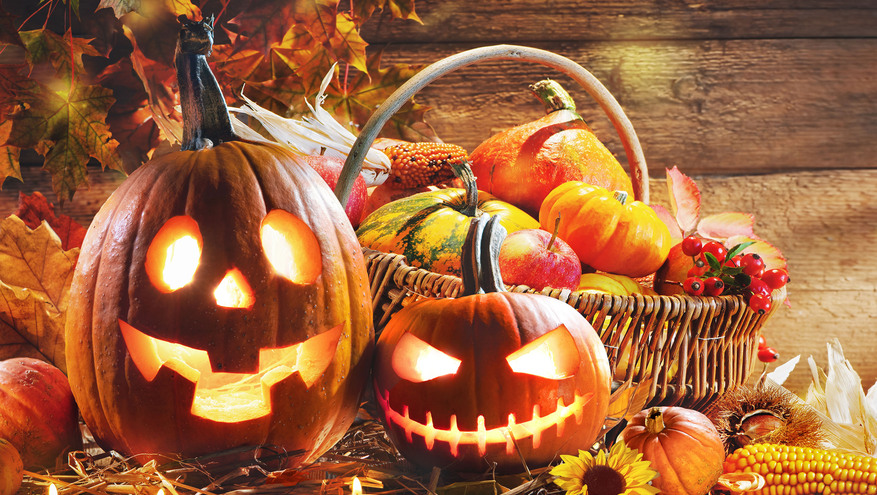 Two carved, jack-o-lanterns part of a fall display with leaves, pumpkins and candles