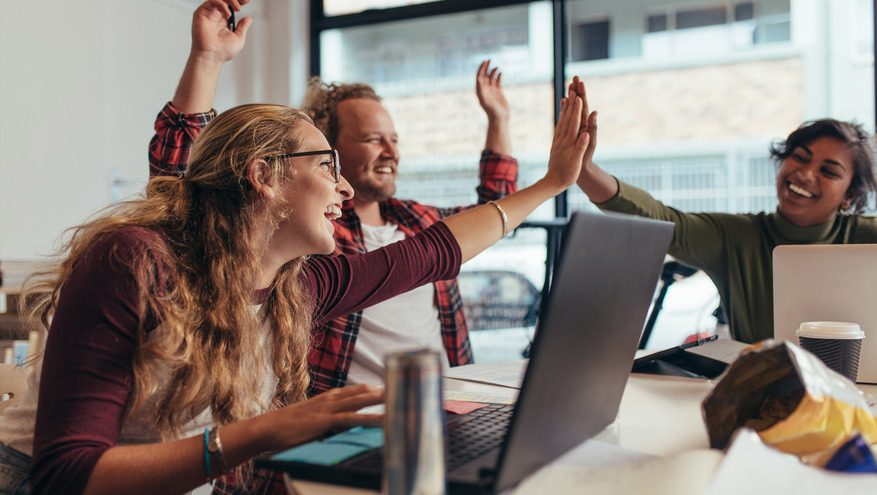 Three team members, two women and a man, high five each other joyfully