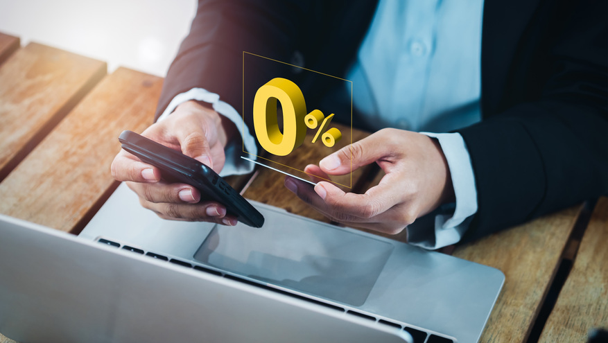 A close-up image of a man's hand holding a credit card while the number "0%" is projected from his laptop