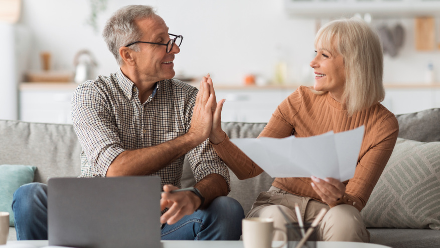 A happy, mature couple give each other a high-five while looking over paperwork