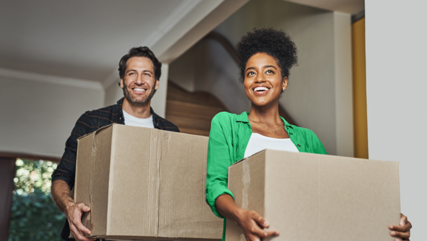 Two new homeowners carry boxes into their new house