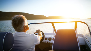 A senior man drives a boat at sunset