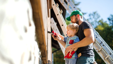 A dad and his young son paint the outside of their house