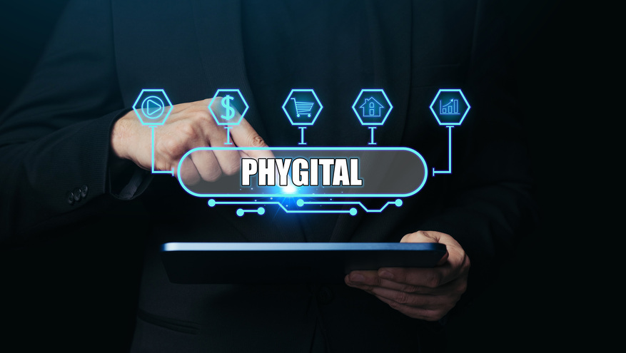 A business person holds a tablet with the word "phygital" and digital icons