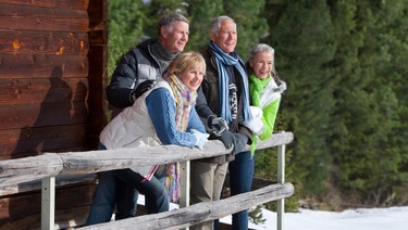 Four individuals relax on the porch of a snowy cabin