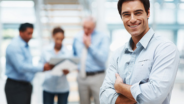 Business man smiling if foreground with three coworkers in background.