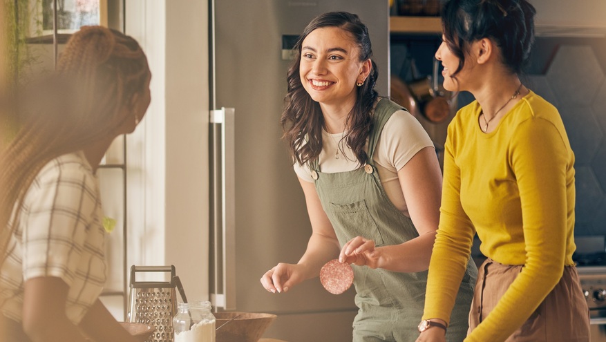 Three female housemates make dinner in their kitchen