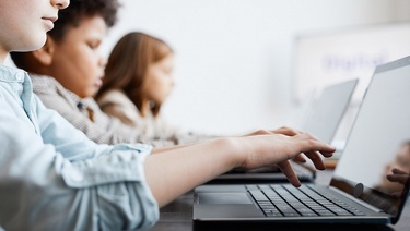 A group of three diverse children work on laptop computers