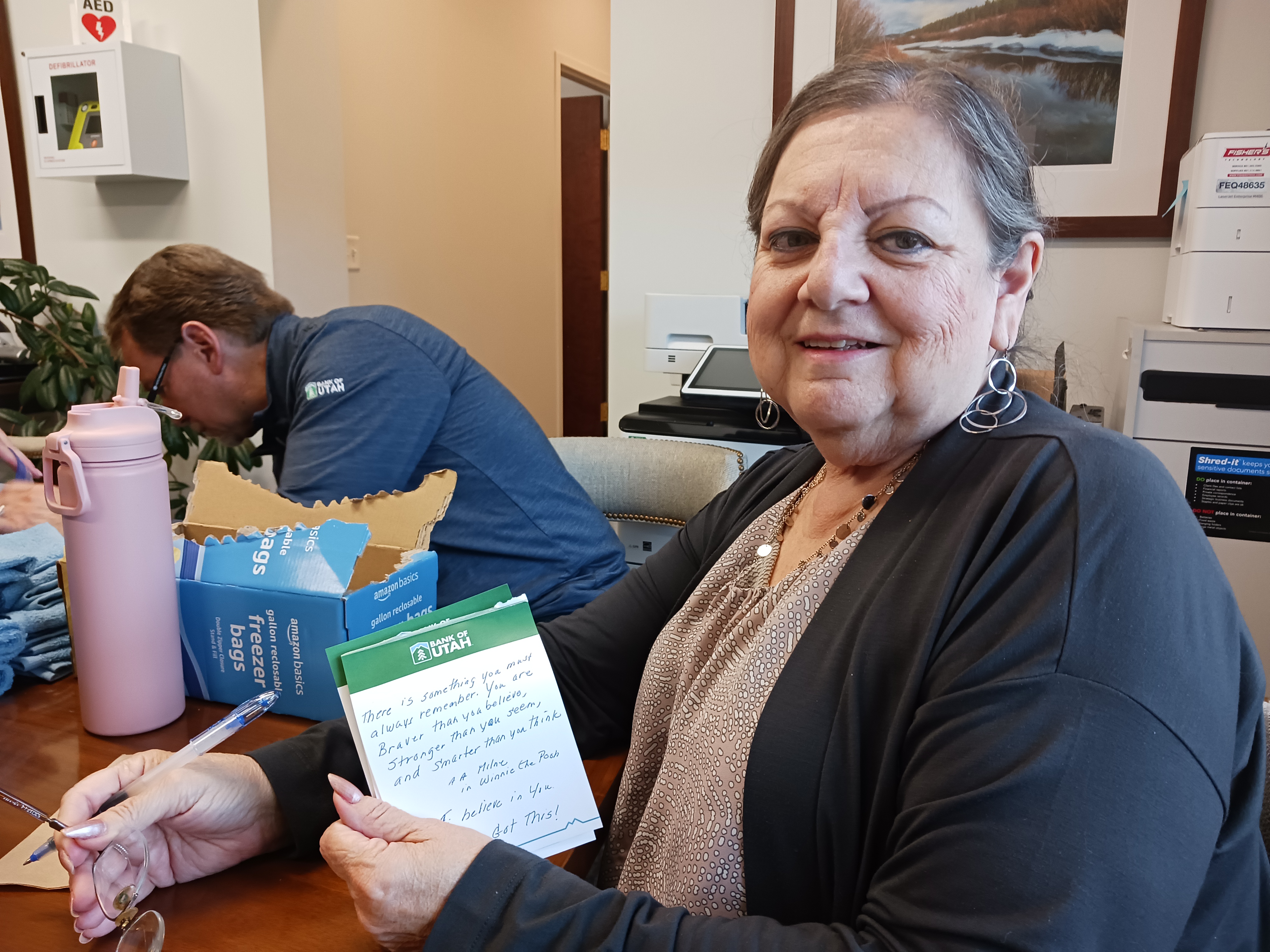 A Bank of Utah team member smiles while holding a handwritten note of encouragement on a branded notepad.
