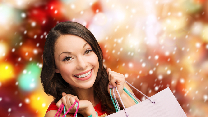 Young woman smiling holding shopping bags with snowflakes in background.