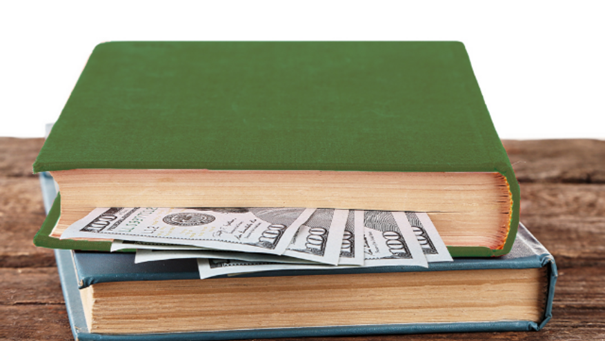 A stack of hardcover books on a wooden table, with hundred-dollar bills tucked midway through the top book. The image uses the metaphor of a book to represent a mid-year financial check-in—pausing halfway through the year to review your financial story.