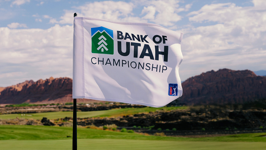 White golf flag with the Bank of Utah Championship logo waving on a green fairway at Black Desert Resort, with red rock mountains in the background.