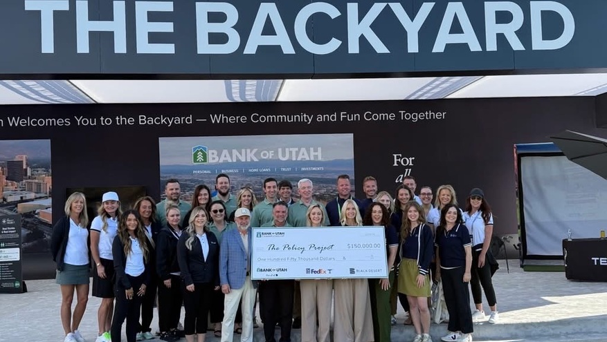 Group photo at the Bank of Utah Championship showing representatives holding a large donation check for The Policy Project in front of “The Backyard” event space.