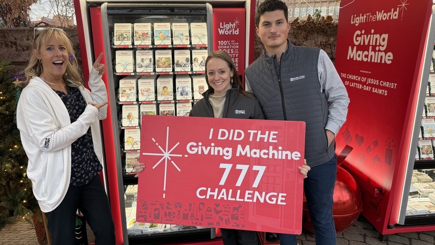 Three Bank of Utah team members stand in front of a Light the World Giving Machine, holding a large sign that reads ‘I Did the Giving Machine 777 Challenge.