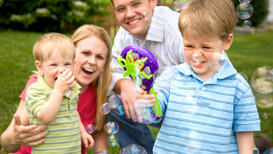 Young couple with two small boys playing with bubbles at a park.