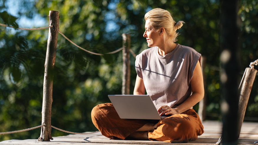 middle aged woman sitting cross-legged using laptop outside