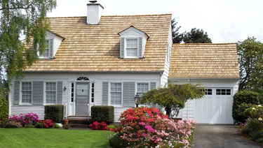 Rambler home with white siding and green lawn with flowers in bloom out front.