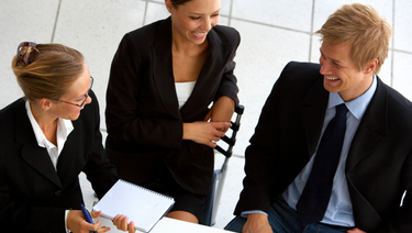 Treasury Management team - Three business people sitting around desk and smiling.