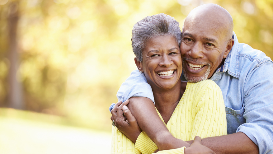 Older couple holding each other and smiling with fall scene in background.