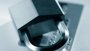 Close up of padlock sitting on top of credit card, image is all gray and white tones.