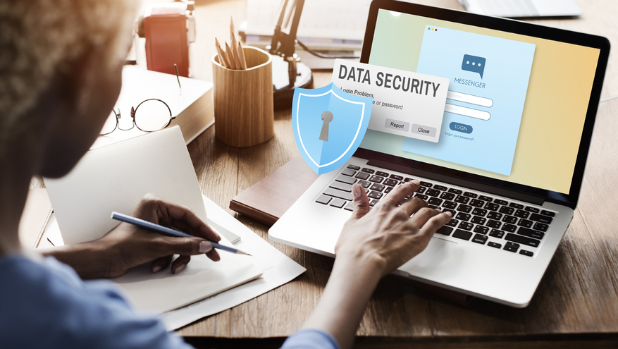 Woman using Apple laptop on desk with Data Security warning and security shield hovering over computer screen.