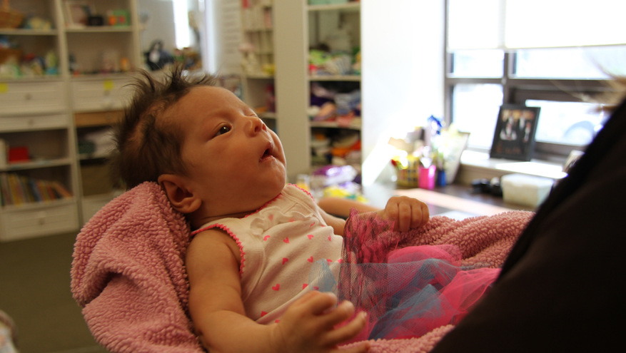 Close up of new born baby girl with dark hair being held in pink blanket.