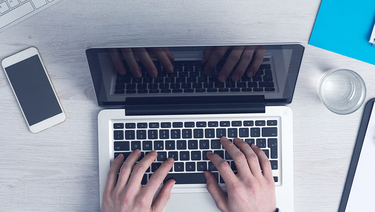 Man's hands on laptop keyboard, working at desk with smartphone and business documents