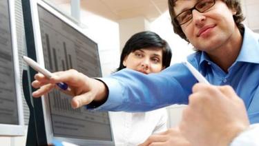 Business men and woman going over charts and graphs on multiple computer monitors.