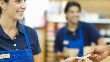 Woman wearing a blue employee type polo shirt and apron with name tag, accepting an employee card from another person.