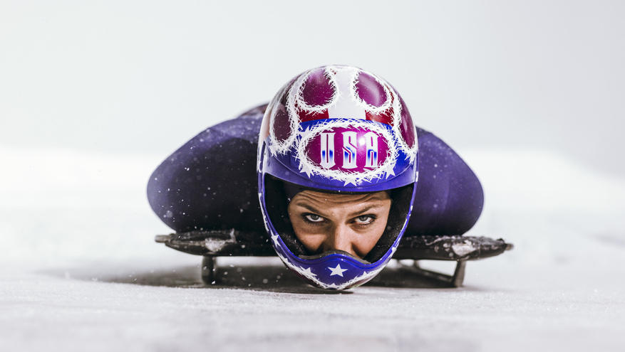 Noelle Pikus-Pace sledding face first on luge sled wearing USA Olympic helmet and uniform.