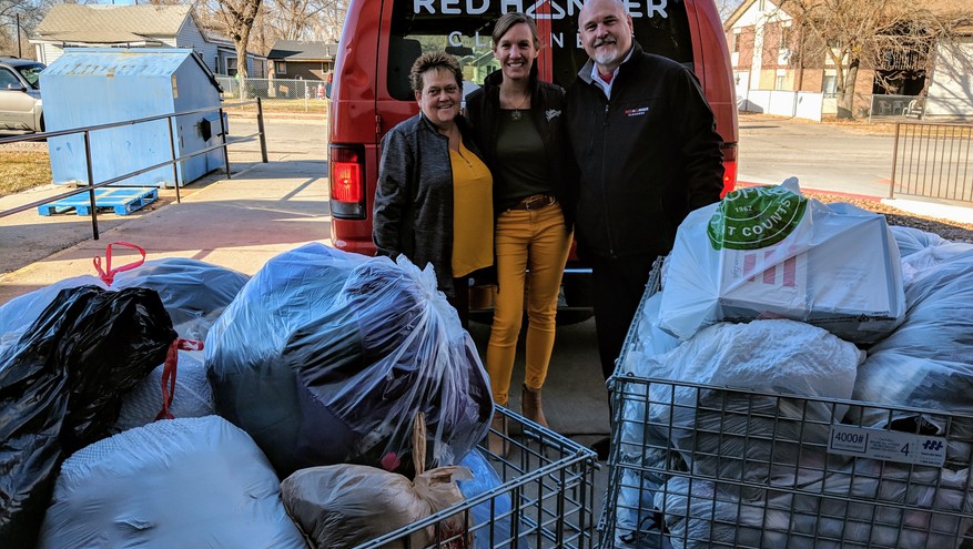 Photo of three people standing by warm clothing donations collected in large bags