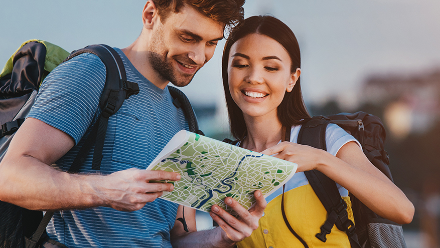 A man and a woman wearing backpacks looking at a map