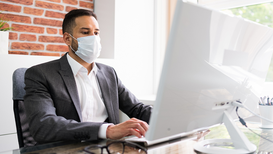 Man wearing a mask working on a computer