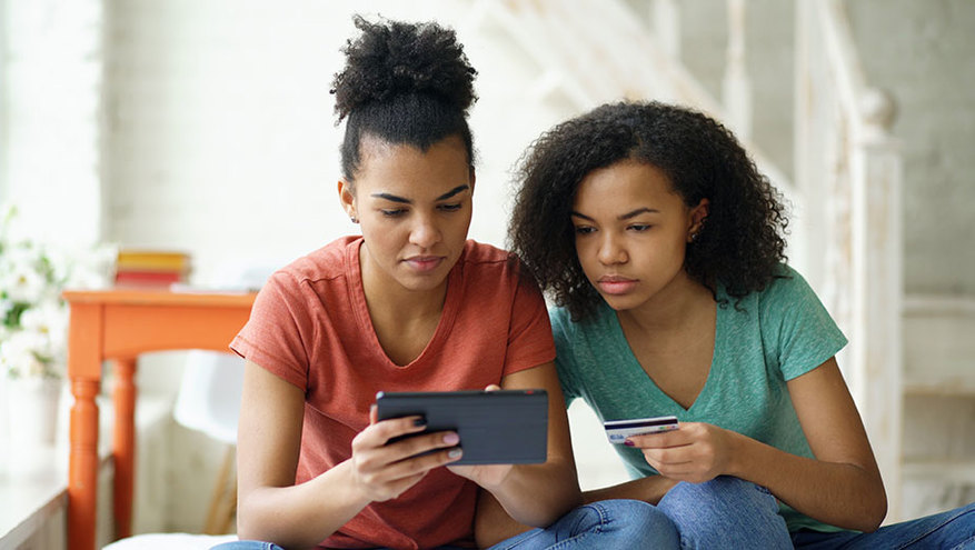 One young woman and one teen girl contemplate making an online purchase, while holding a debit card