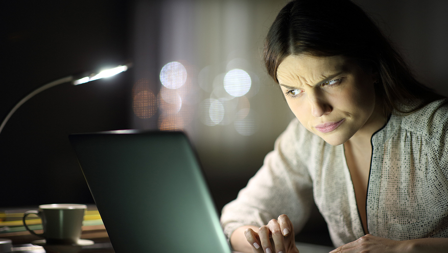 A young woman looks at her computer screen with a confused, doubtful expression on her face