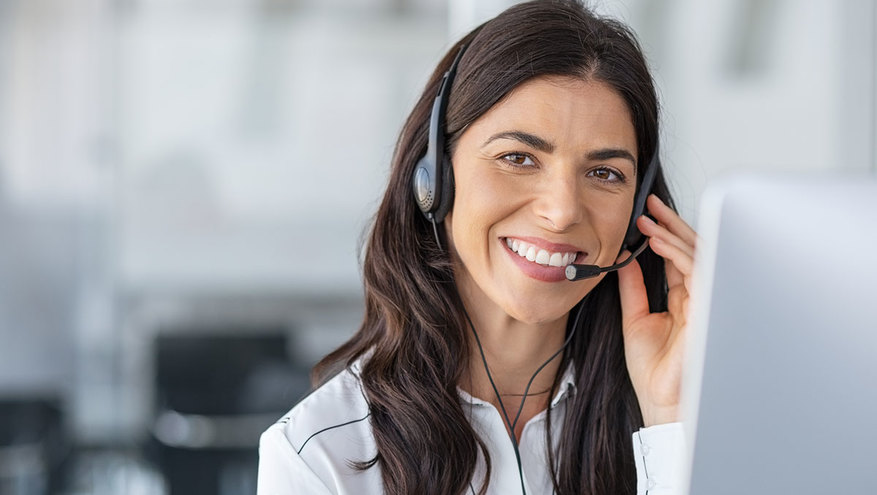 A smiling, professional woman in a headset sits in front of a computer