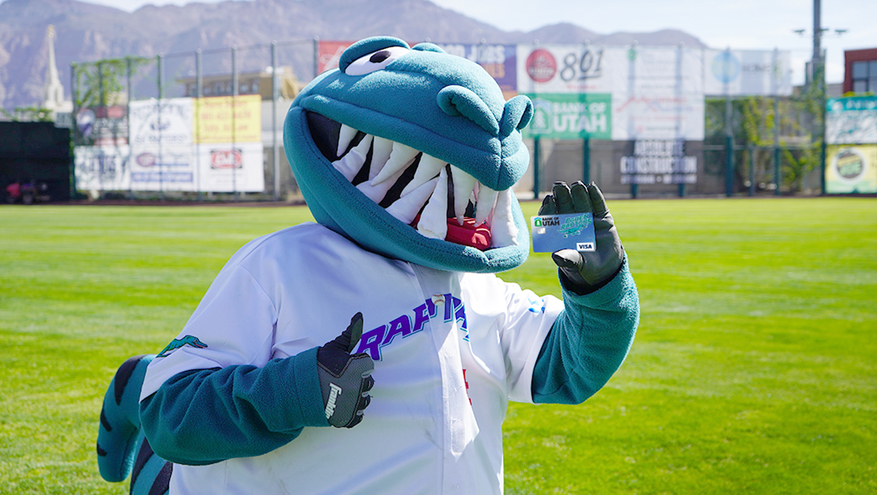 Ogden Raptor baseball team's dinosaur mascot holds up a Bank of Utah debit card